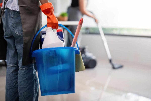 Office cleaner carrying bucket with cleaning supplies and vacuuming. Concept of workplace organization