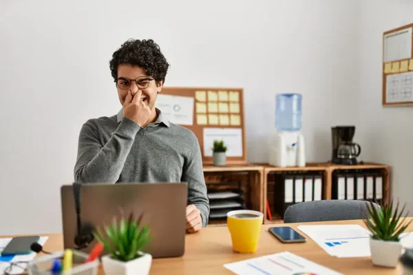 Smelly office | Man holding his nose in the office